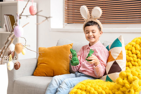 Cute little boy with bunny ears and toy rabbits sitting on sofa at home