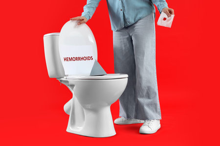 Mature woman with bloody paper and thumbtack on toilet bowl against red background. Hemorrhoids conceptの写真素材