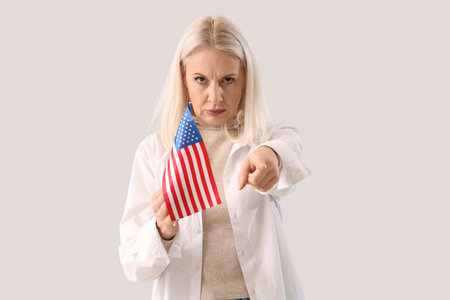 Mature woman with USA flag pointing at viewer on light background. Accusation conceptの写真素材