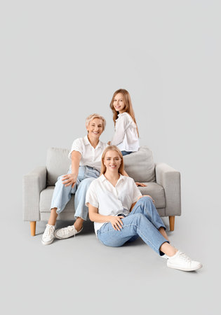 Little girl with her mom and grandmother sitting on sofa against light background