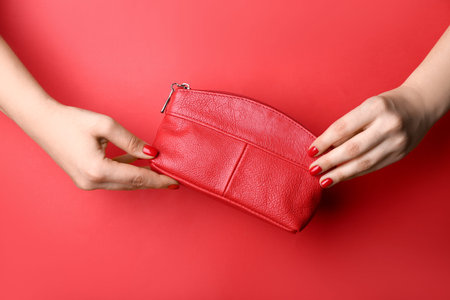 Female hand with stylish red manicure holding bag on color background
