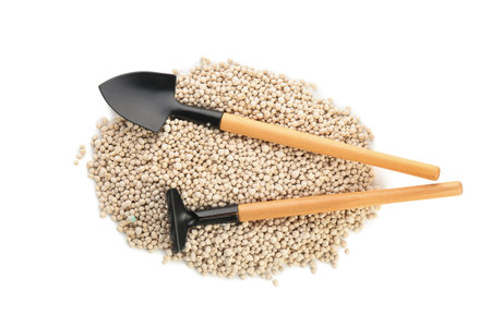 Gardening shovel and rake with granular fertilizer isolated on white background