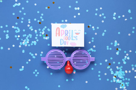 Festive postcard for April Fools Day with funny glasses and confetti on blue background