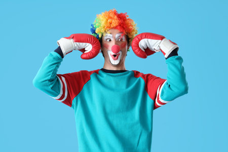 Portrait of surprised clown with boxing gloves on blue background. April Fool's day celebration