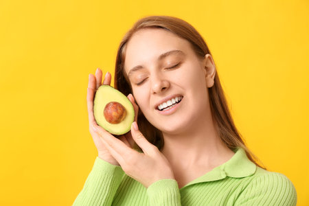 Pretty young woman with avocado on yellow background