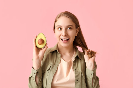 Pretty young woman with avocado on pink background