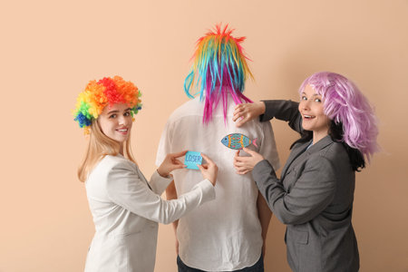 Young women sticking papers on their colleague's back against beige background. April Fools' Day celebrationの写真素材