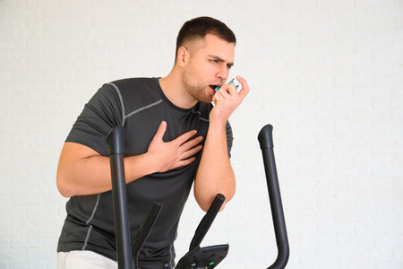 Sporty young man using inhaler on exercise bike in gymの写真素材