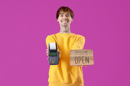Young online store seller with payment terminal and OPEN sign on purple background