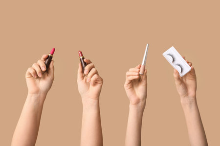 Female hands with lipsticks, fake lashes and eyeliner on beige backgroundの写真素材
