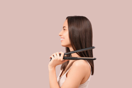 Beautiful young woman with hair straightener on pink background