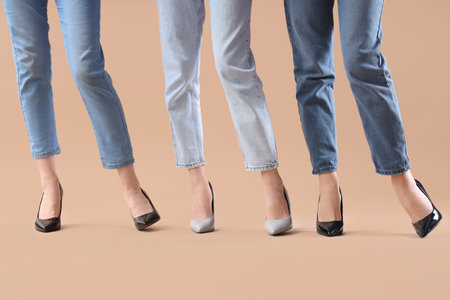 Female legs wearing different high heeled shoes on beige background