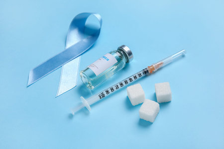 Awareness ribbon with insulin, syringe and sugar cubes on blue background. Diabetes concept
