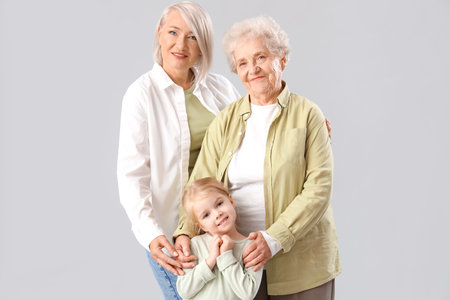 Little girl with her grandmother and great-grandma on light background