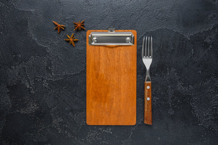 Wooden menu board, fork and anise stars on dark background