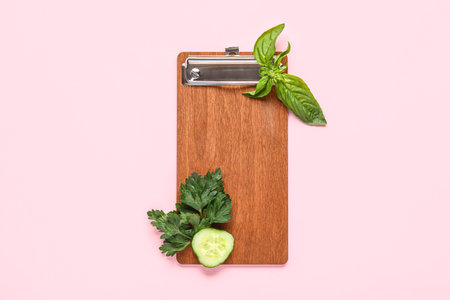 Composition with wooden menu board, parsley, basil and cucumber slice on pink backgroundの写真素材