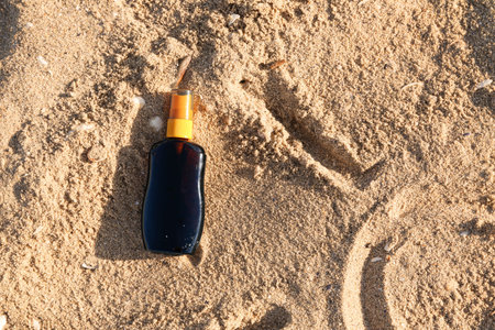 Bottle of sunscreen cream on sand at sea beach