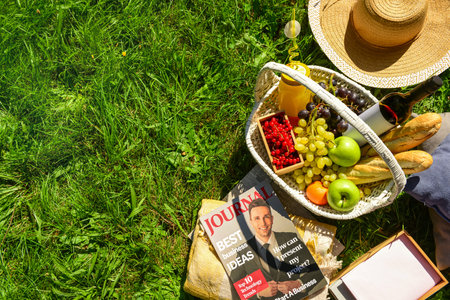 Set for romantic picnic with wicker basket full of tasty food and drinks on grass in parkの写真素材