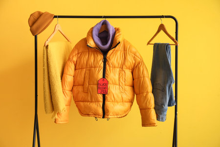 Rack with different clothes on yellow background. Black Friday sale