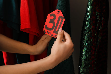 Female hands with different clothes and sale tag, closeup. Black Friday