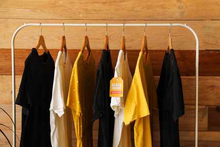 Rack with different clothes near wooden wall, closeup. Black Friday sale
