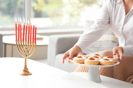 Young woman with donuts celebrating Hanukkah with menorah at home, closeup