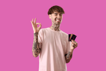 Tattooed young man with credit cards showing OK on purple backgroundの写真素材