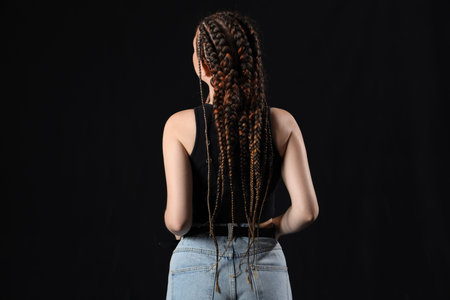 Young woman with dreadlocks on dark background, back view