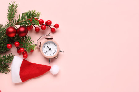 Alarm clock and Santa hat, Christmas tree branches with balls on pink background