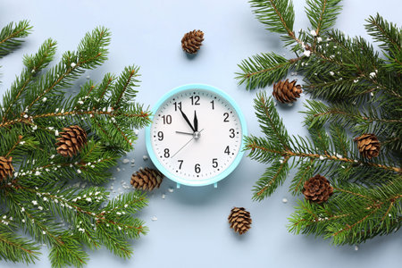 Alarm clock and Christmas tree branches with cones on blue background