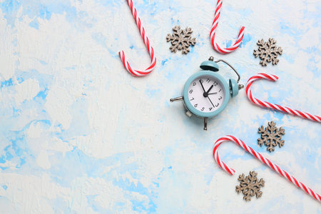 Alarm clock with Christmas candy canes and snowflakes on light blue background