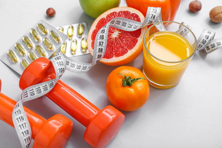 Composition with dumbbells, measuring tape, pills and healthy food on gray background, closeup