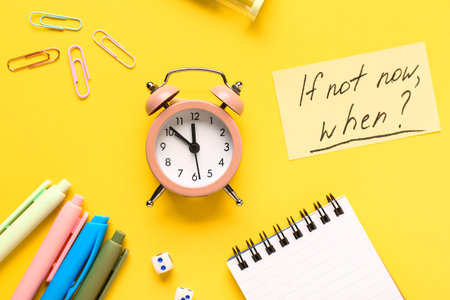 Text IF NOT NOW, WHEN? with alarm clock, paper clips and pens. Time management. Top view