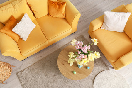 Interior of modern living room with flowers, Easter eggs and bunny on coffee table, top view