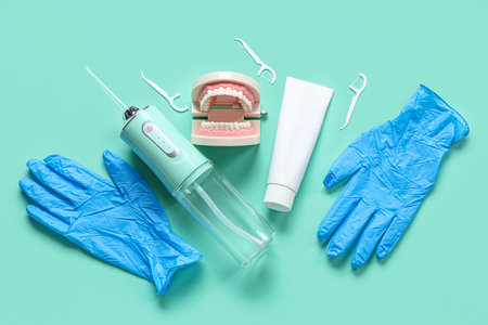Medical gloves, oral irrigator, jaw model and toothpaste on turquoise background