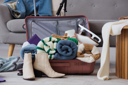 Open suitcase with warm clothes and travel accessories in room