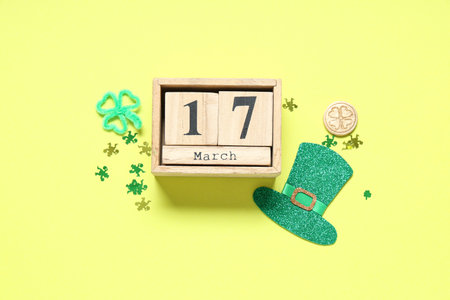 Paper leprechaun hat with calendar and decor for St. Patrick's Day on yellow background