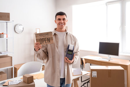 Male online store seller with OPEN sign and payment terminal in warehouse
