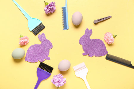 Frame made of paper bunnies with Easter eggs, hairdressing accessories and flowers on yellow backgroundの写真素材
