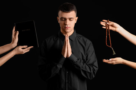 Young man praying and hands holding rosary beads with Bible on black background