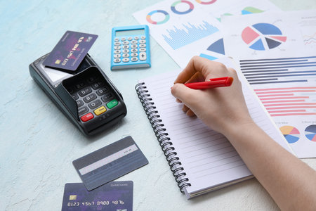 Female hand with notebook, calculator, credit cards and charts on light blue background. House rent...