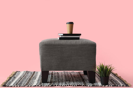 Coffee cup with books on soft pouf against pink backgroundの写真素材