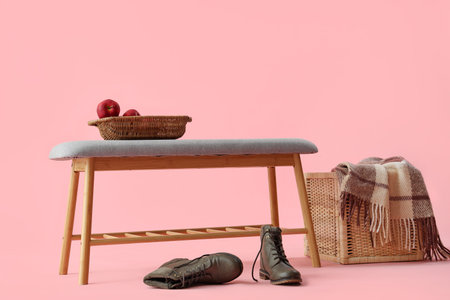Soft bench with apples, shoes and basket on pink background