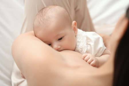 Young woman breastfeeding her baby in bedroom, closeup