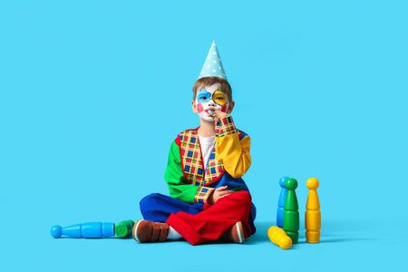 Funny little boy in clown costume with party whistle and juggling clubs on blue background. April Fools' Day celebrationの写真素材