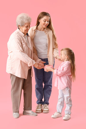 Little girl giving her mother and great-grandma gift on pink backgroundの写真素材