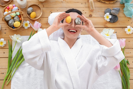Young woman with Easter eggs and tulips lying on table in spa salon, top view