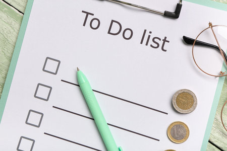 Clipboard with to do list, eyeglasses and coins on green wooden background. Time management concept....