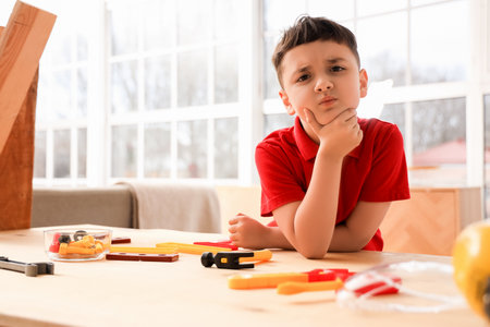 Thoughtful little builder at table with toy tools in roomの写真素材