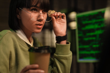 Female programmer with coffee cup working with computer in office at night, closeup